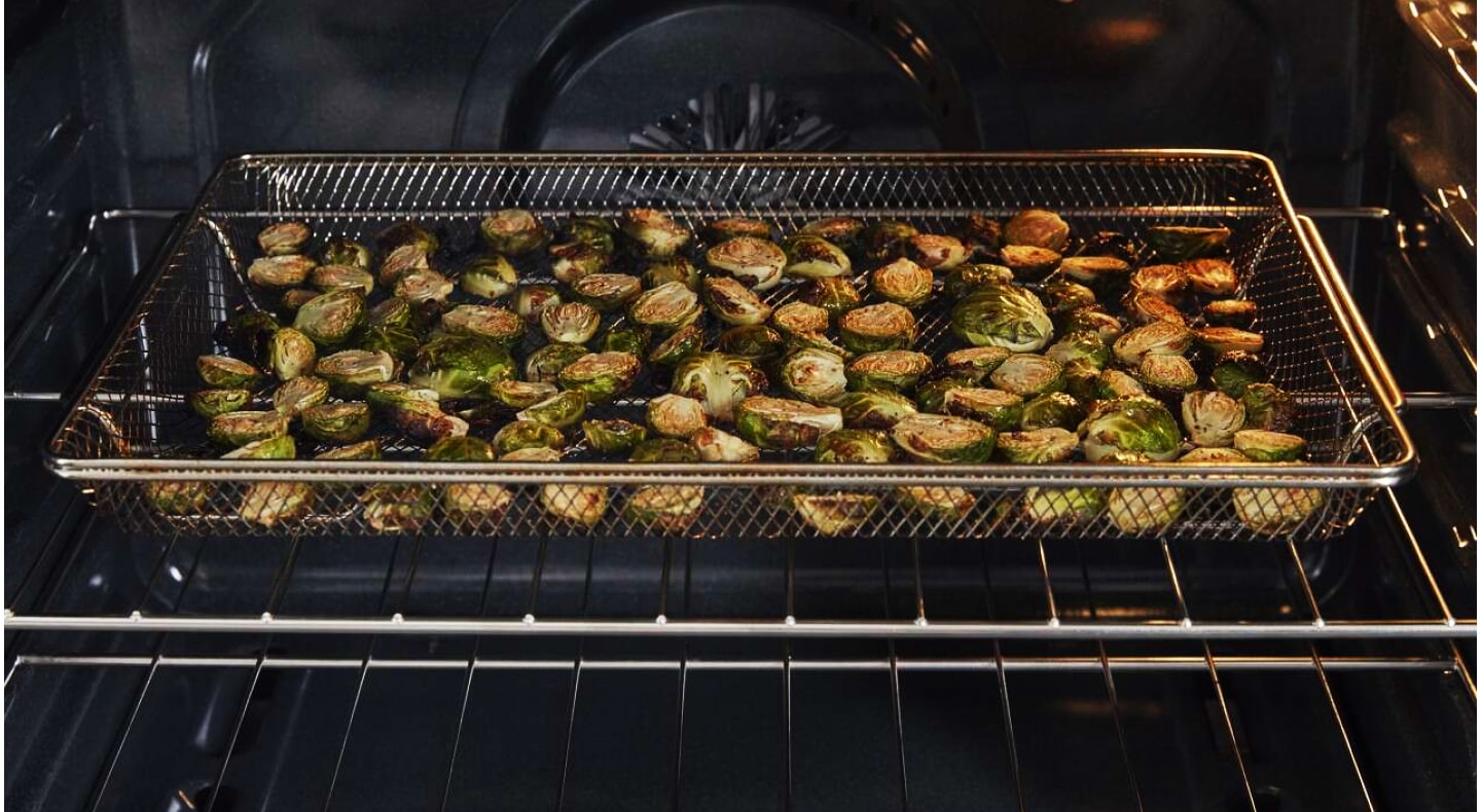Air fryer basket with brussels sprouts inside an oven