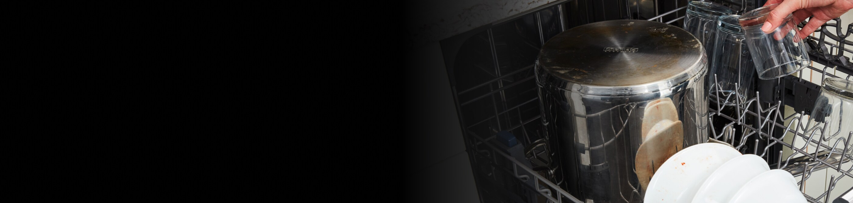 A metal stock pot and other dirty dishes loaded in a dishwasher rack