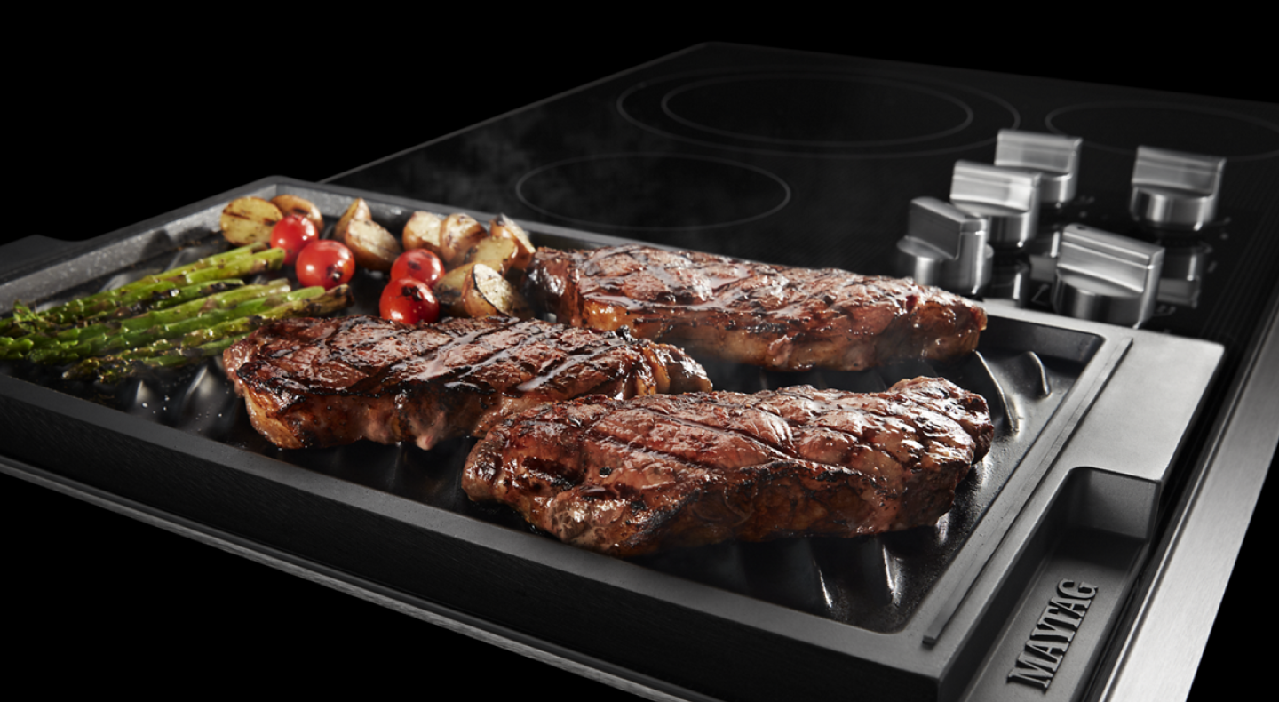 Steak and vegetables cooking on a Maytag® grill pan
