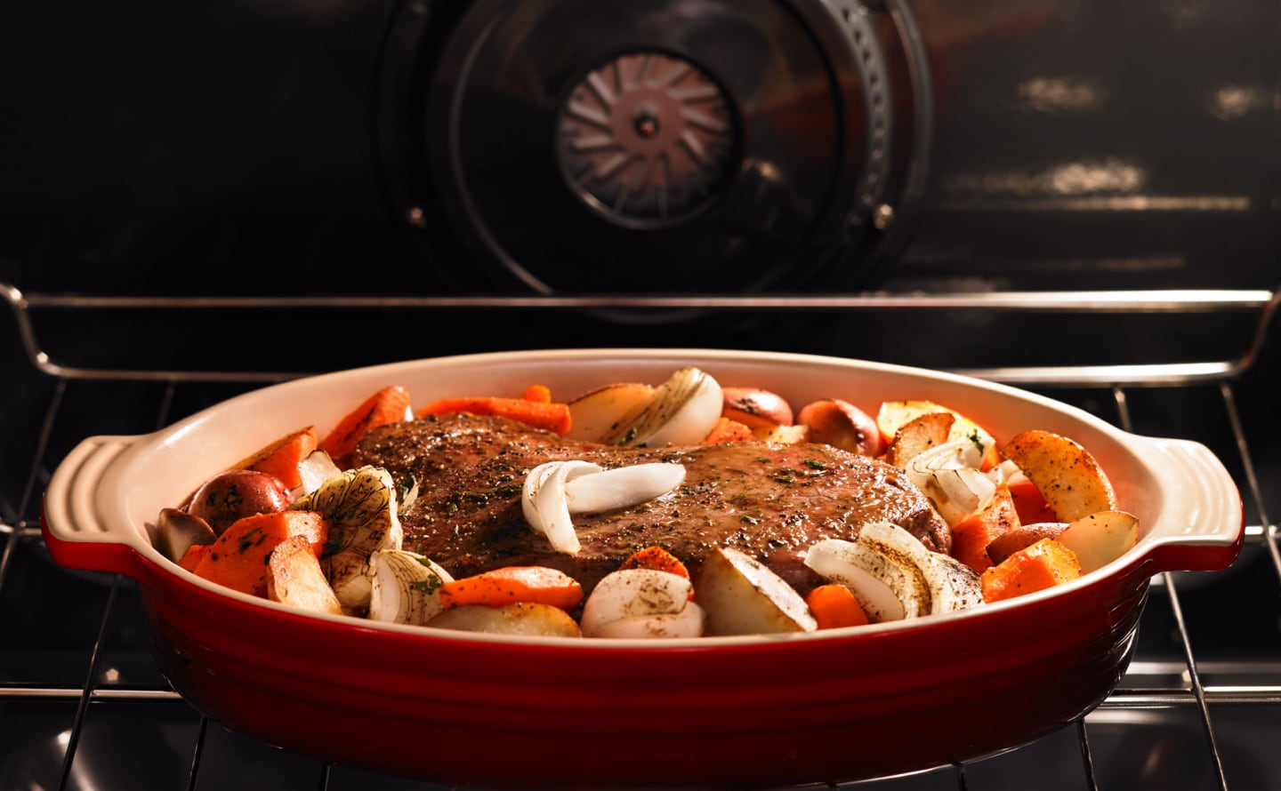 Meat with roasted vegetables cooking in a red baking dish Meat with roasted vegetables cooking in a red baking dish