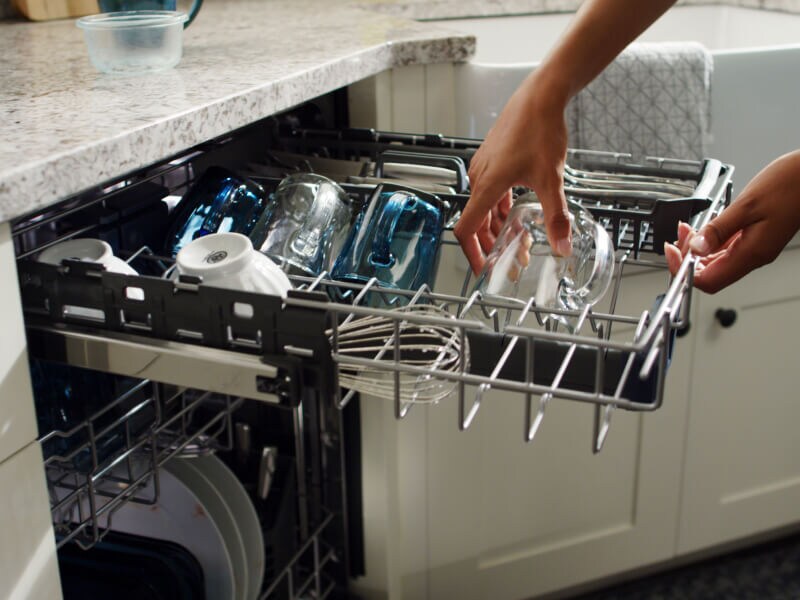 Person loading glasses on a dishwasher third rack