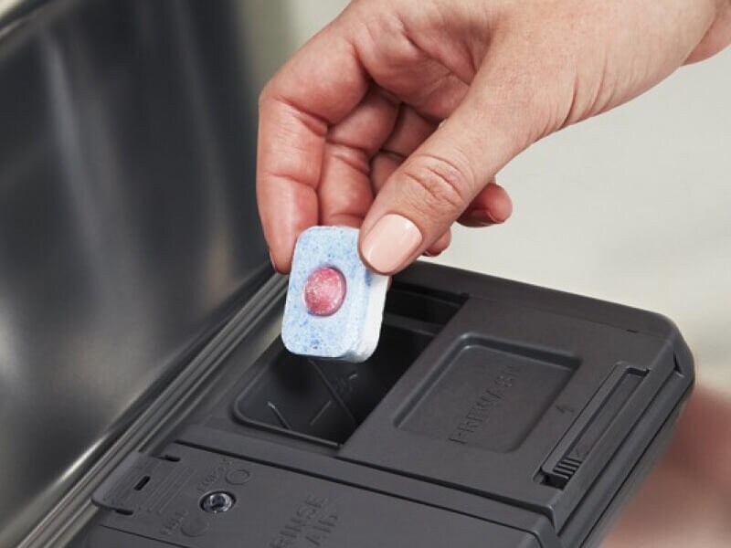 Person placing tablet in dishwasher dispenser