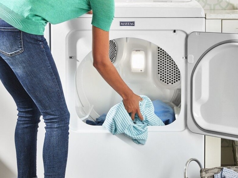 User adding clothes to white front load dryer User adding clothes to white front load dryer