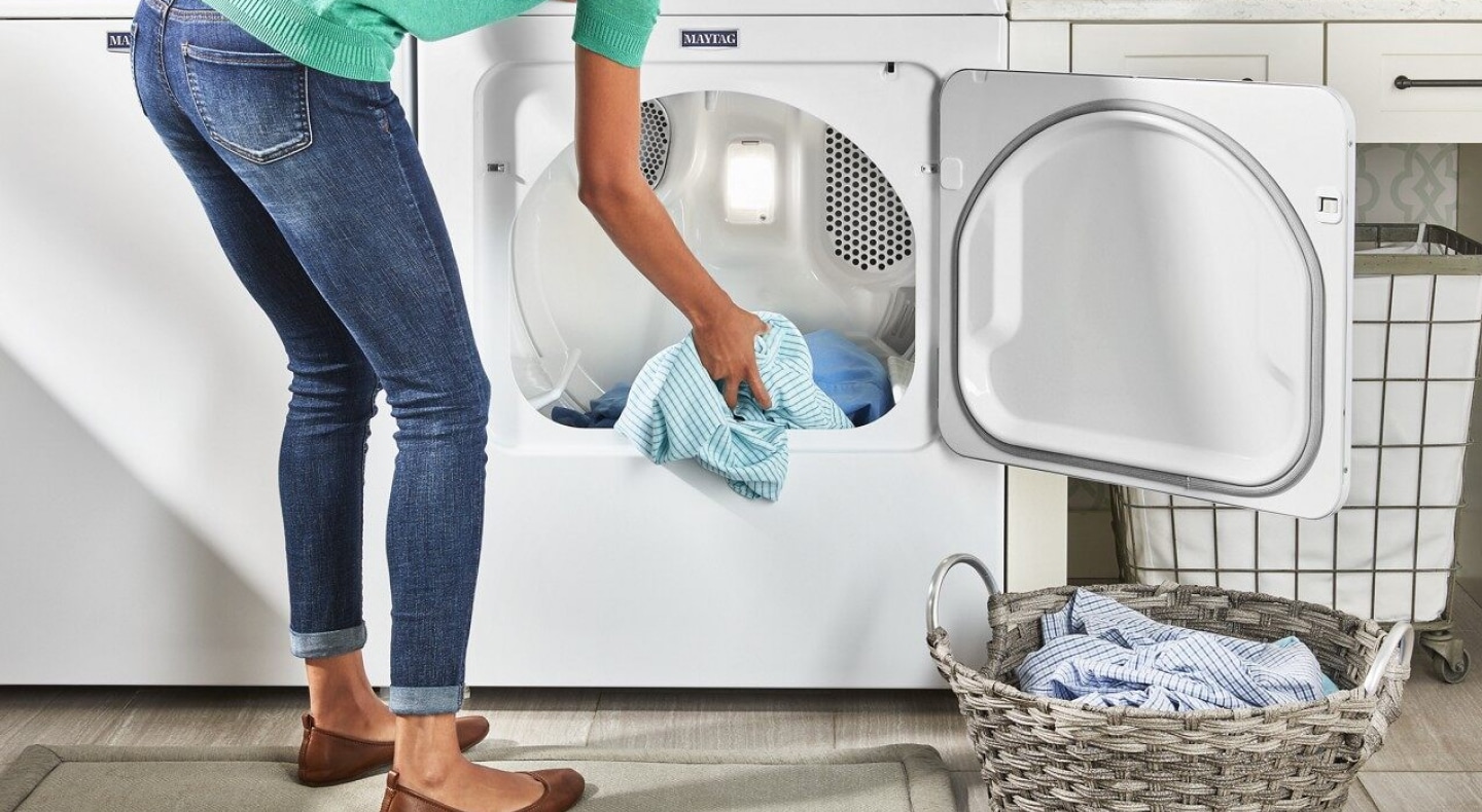 User adding clothes to white front load dryer User adding clothes to white front load dryer