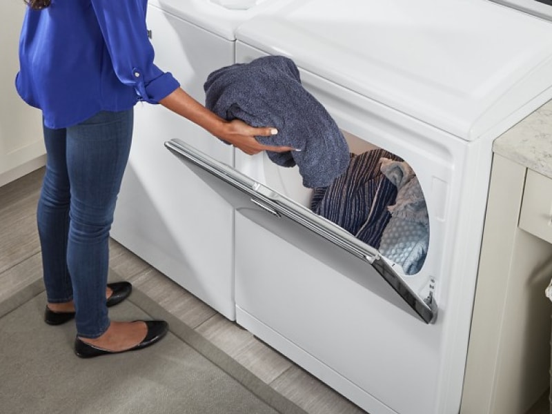 User transferring clothes from white top load washer to white front load dryer User transferring clothes from white top load washer to white front load dryer