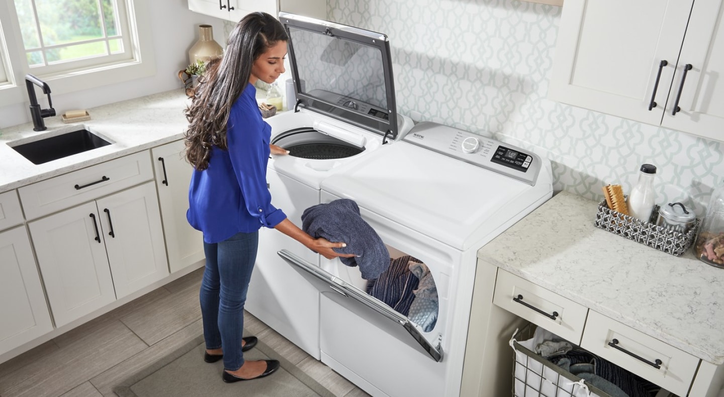 User transferring clothes from white top load washer to white front load dryer User transferring clothes from white top load washer to white front load dryer