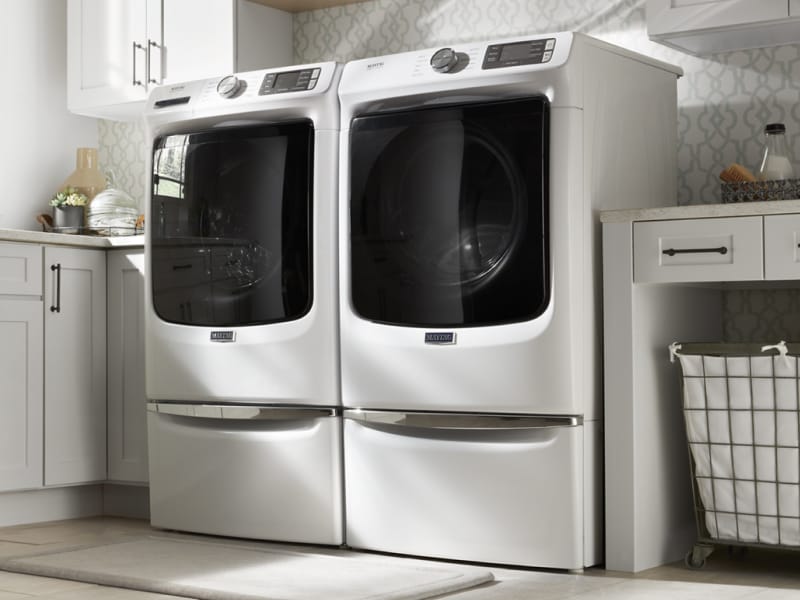 Side-by-side white Maytag® front load washer and dryer on pedestals in laundry room Side-by-side white Maytag® front load washer and dryer on pedestals in laundry room