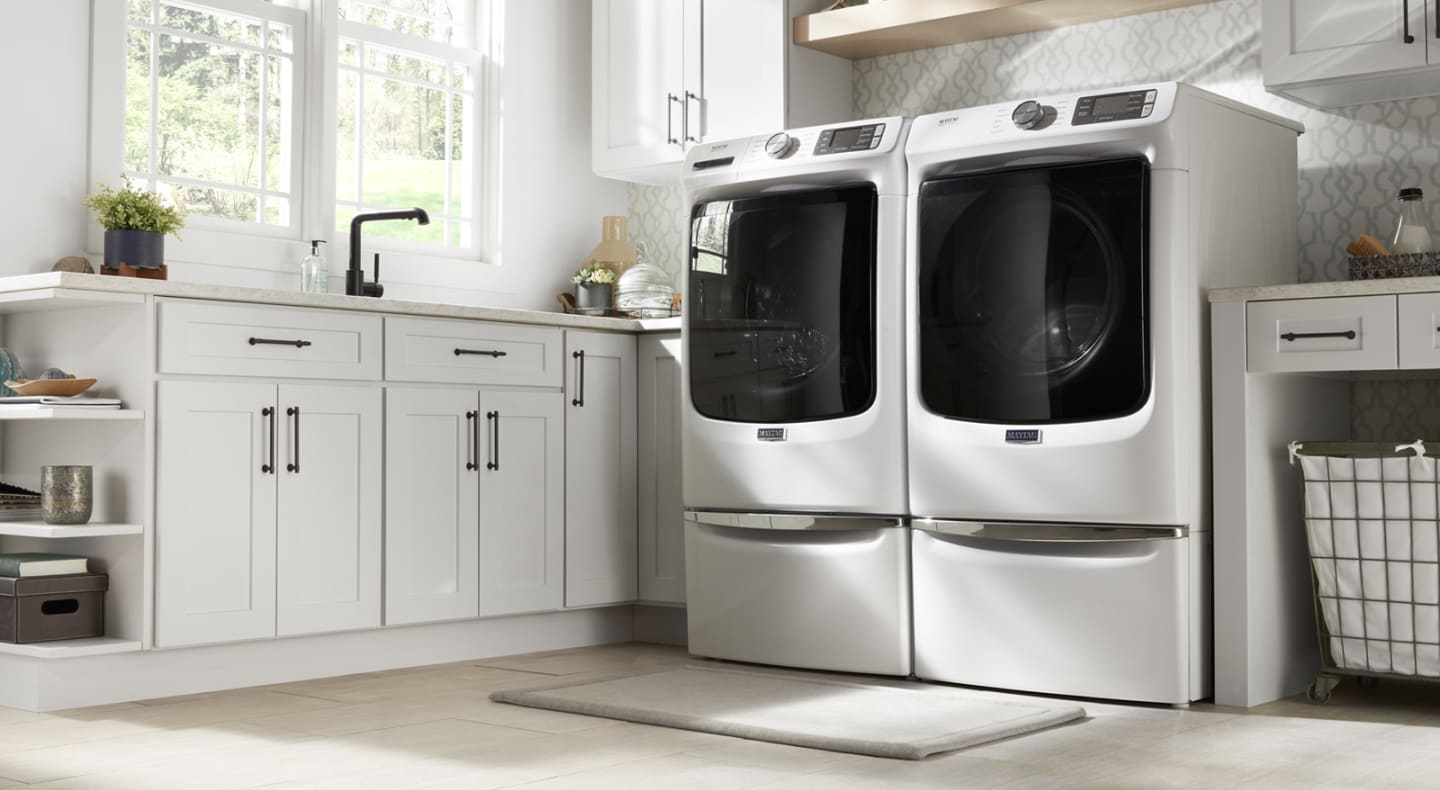 Side-by-side white Maytag® front load washer and dryer on pedestals in laundry room Side-by-side white Maytag® front load washer and dryer on pedestals in laundry room