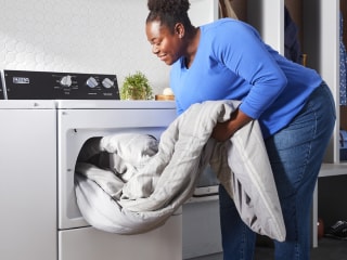 Person loading a comforter in a top load dryer