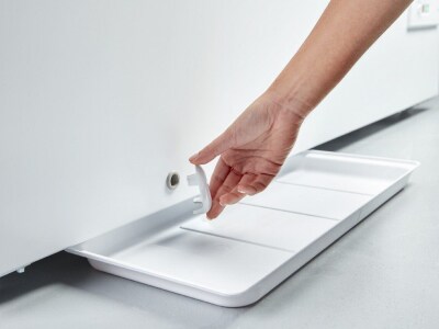 Person unplugging drainage plug at the base of a deep freezer