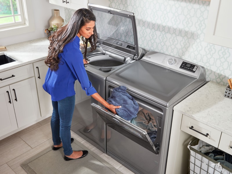 Woman loading landry into a white front loading dryer Woman loading landry into a white front loading dryer