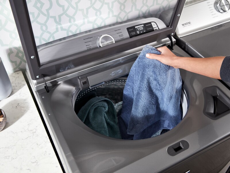 Laundry being added to a metallic slate Maytag® top loading washer Laundry being added to a metallic slate Maytag® top loading washer