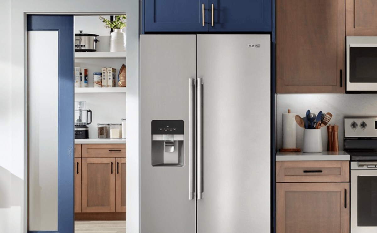 A Maytag brand refrigerator with a stainless steel exterior and ice maker shown inside a dark kitchen