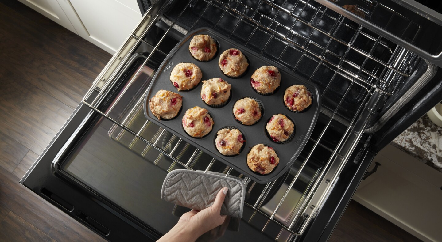 Close-up of a person pulling out freshly baked berry muffins from the middle tray of an oven. Close-up of a person pulling out freshly baked berry muffins from the middle tray of an oven.