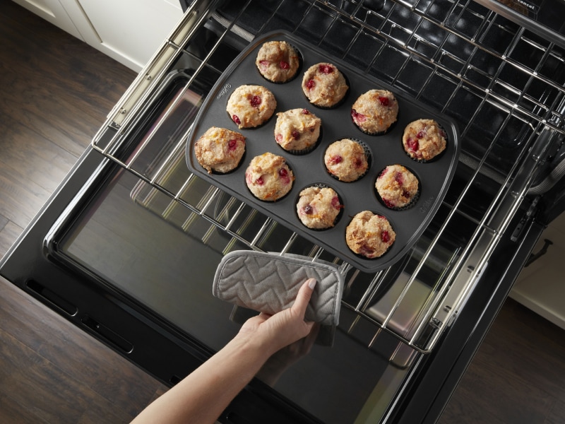 Close-up of a person pulling out freshly baked berry muffins from the middle tray of an oven. Close-up of a person pulling out freshly baked berry muffins from the middle tray of an oven.