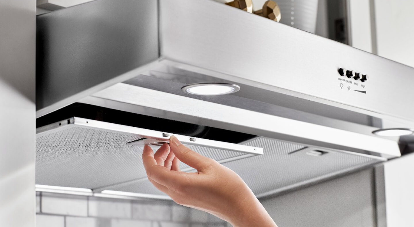 A person opening a grease filter panel on a stainless steel raneg hood