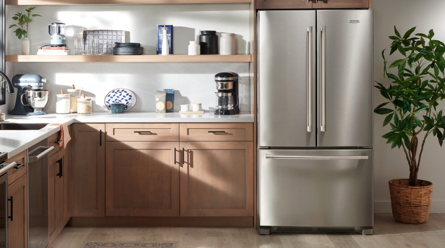 A Maytag® French door refrigerator next to wooden kitchen cabinets