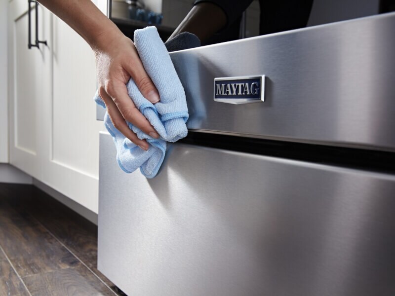 Person wiping the stainless steel of a Maytag® range