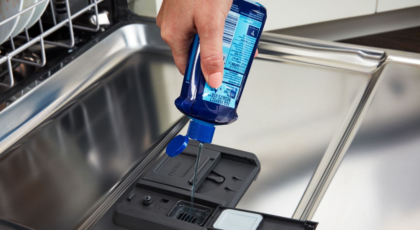 Person adding liquid dish detergent to a dishwasher Person adding liquid dish detergent to a dishwasher