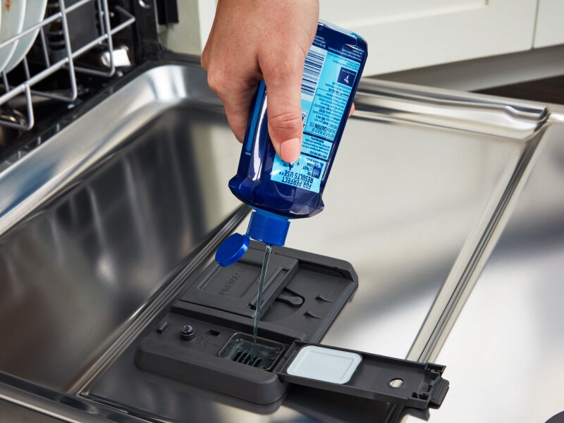 Person adding liquid dish detergent to a dishwasher Person adding liquid dish detergent to a dishwasher