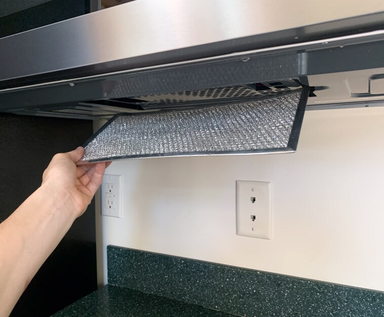 Hand removing grease filter from bottom of the microwave