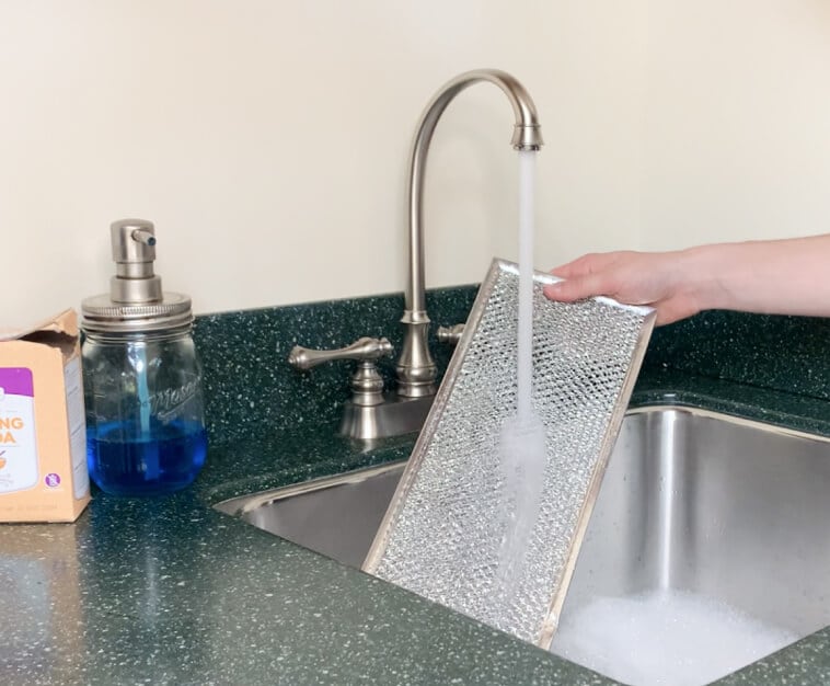 Grease filter being rinsed under a running faucet