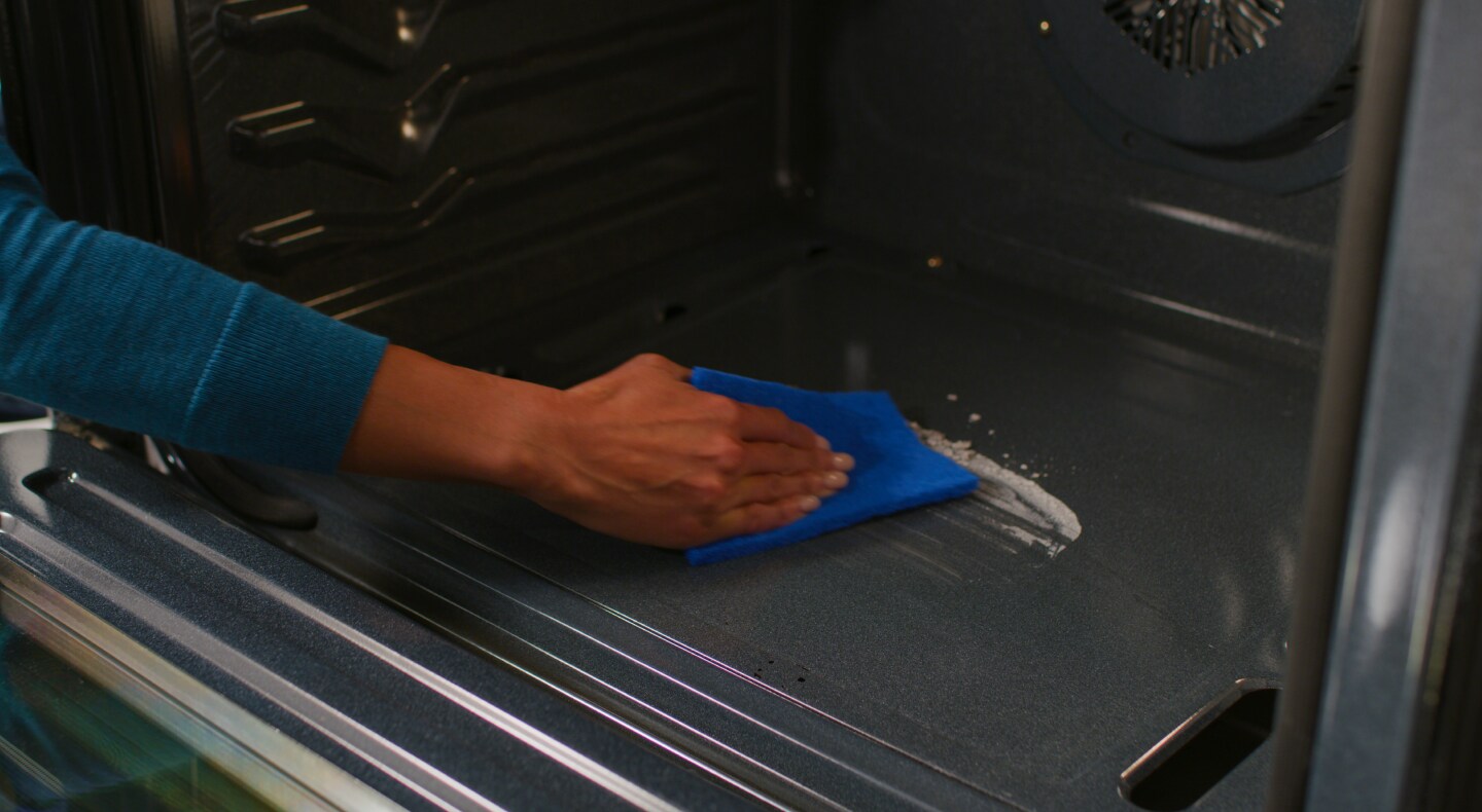 Person wiping up cleaner on the bottom of an oven Person wiping up cleaner on the bottom of an oven