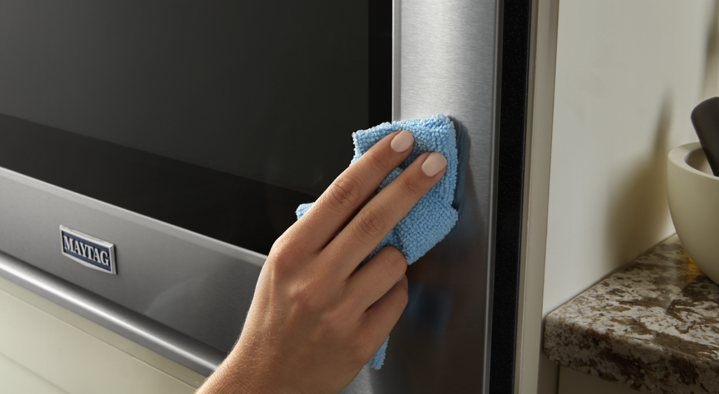 A person wipes down the stainless steel exterior of a Maytag® oven. A person wipes down the stainless steel exterior of a Maytag® oven.