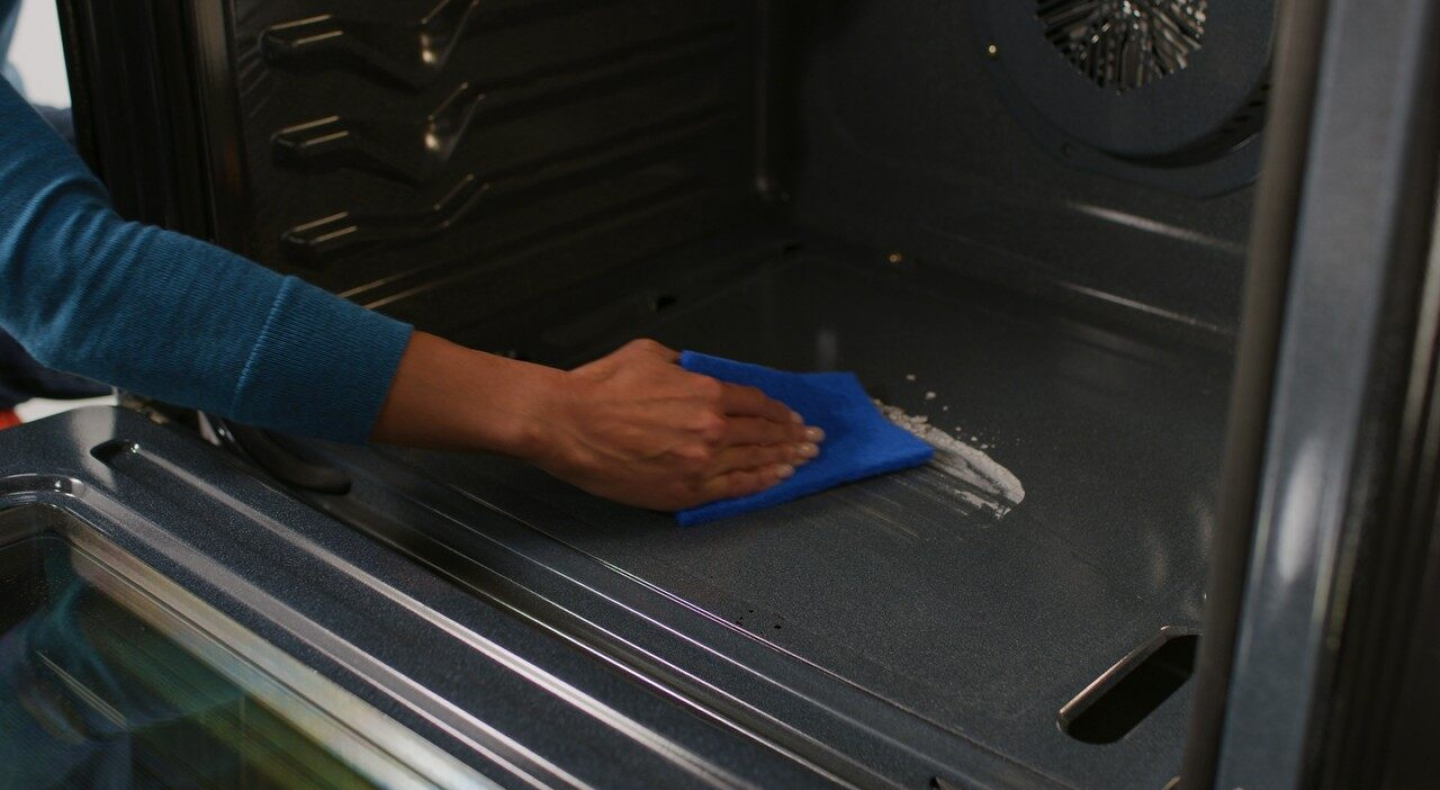 A person wipes down the bottom of an oven. A person wipes down the bottom of an oven.
