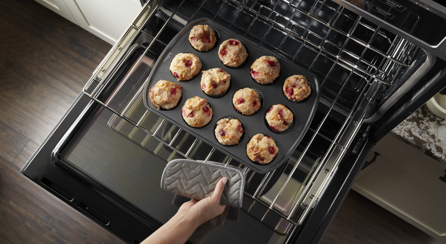 Person pulling rack from oven with muffin pan Person pulling rack from oven with muffin pan