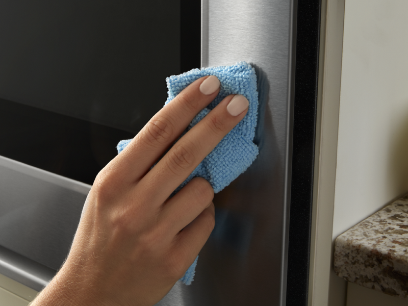 A person wipes down the stainless steel exterior of a Maytag® oven.