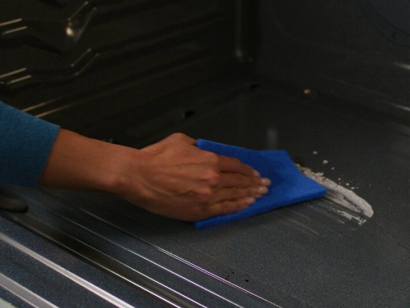 A person wipes down the bottom of an oven. A person wipes down the bottom of an oven.