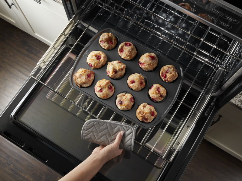 Person pulling rack from oven with muffin pan Person pulling rack from oven with muffin pan