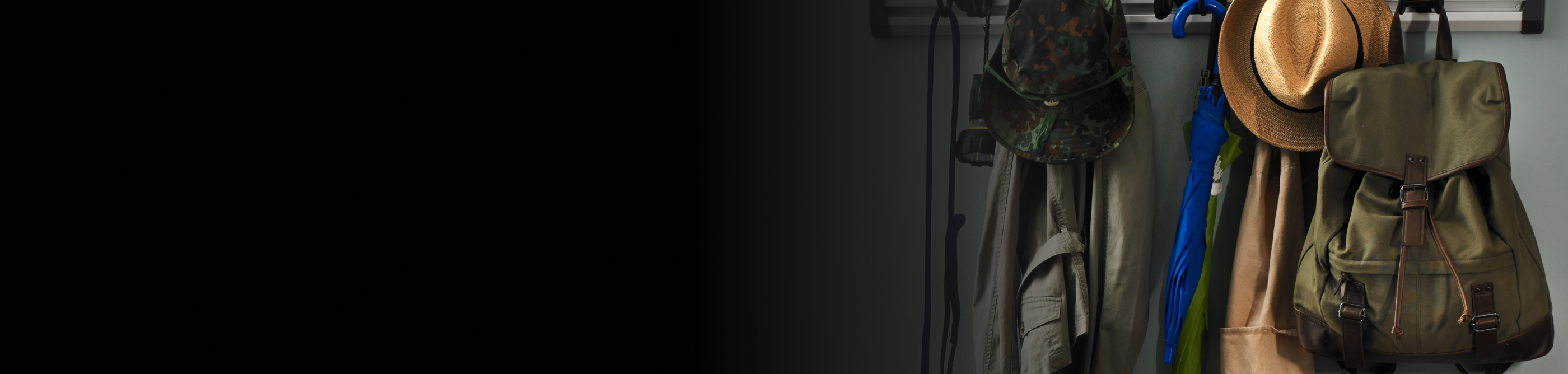 A closeup of a coat rack with jackets, a canvas backpack and hat.