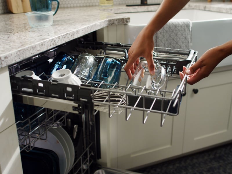 Person placing glasses on third-level rack of dishwasher Person placing glasses on third-level rack of dishwasher
