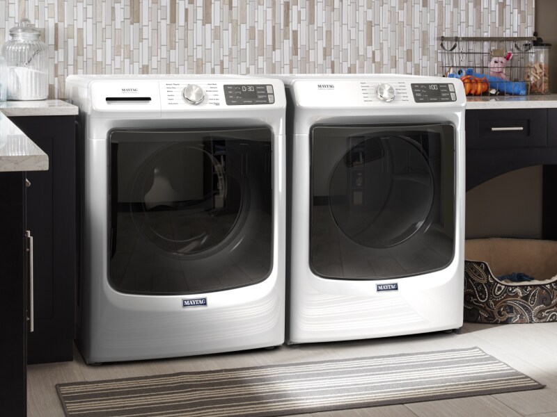 White Maytag® front load washer and dryer side by side in laundry room with dark cabinets White Maytag® front load washer and dryer side by side in laundry room with dark cabinets