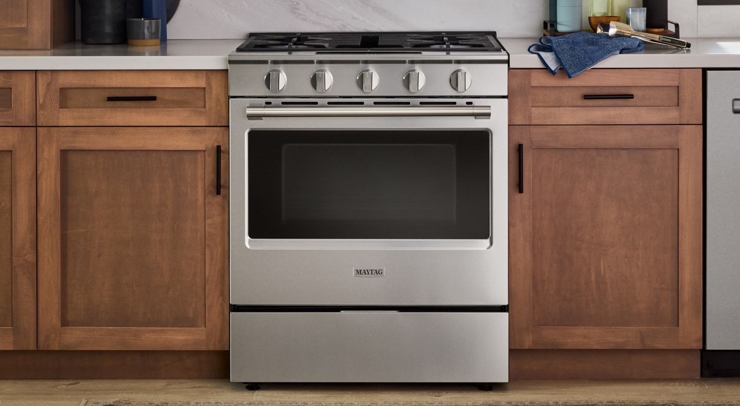 A gas slide-in range in a kitchen with natural wood cabinetry