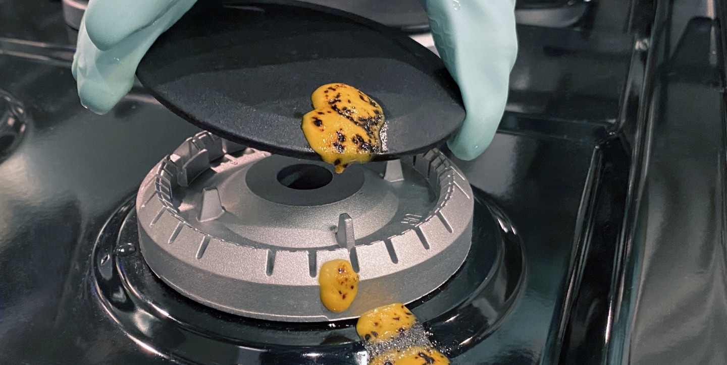 Hand removing the cap from a burner with cheese spilled on it