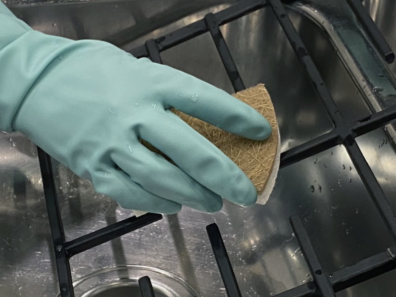 Gloved hand scrubbing range grates with a sponge