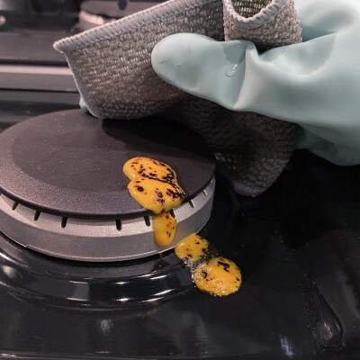 Hand wiping cheese off gas burner cap