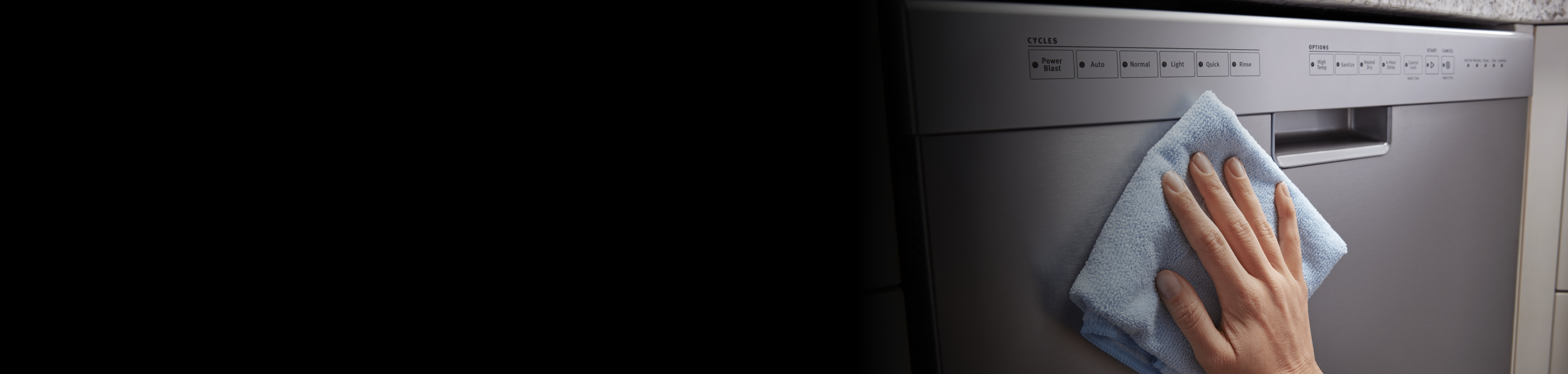 Person wiping down the door panel of a stainless steel dishwasher