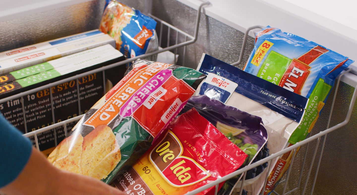Person adjusting baskets filled with frozen food inside of chest freezer Person adjusting baskets filled with frozen food inside of chest freezer