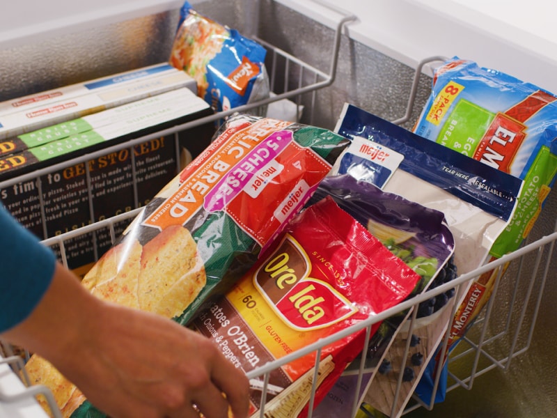 Person adjusting baskets filled with frozen food inside of chest freezer Person adjusting baskets filled with frozen food inside of chest freezer