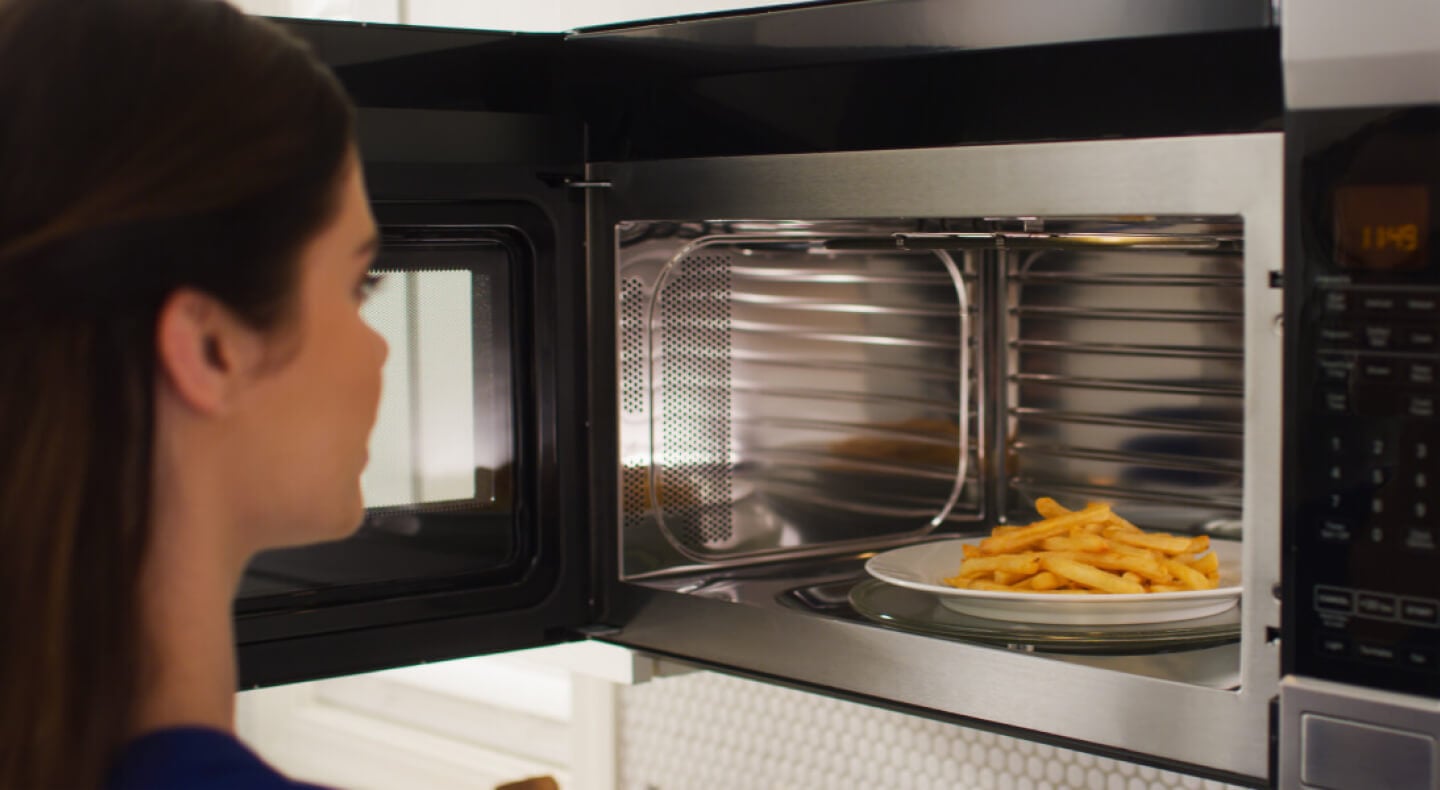 A person removing plate of fries from a microwave A person removing plate of fries from a microwave