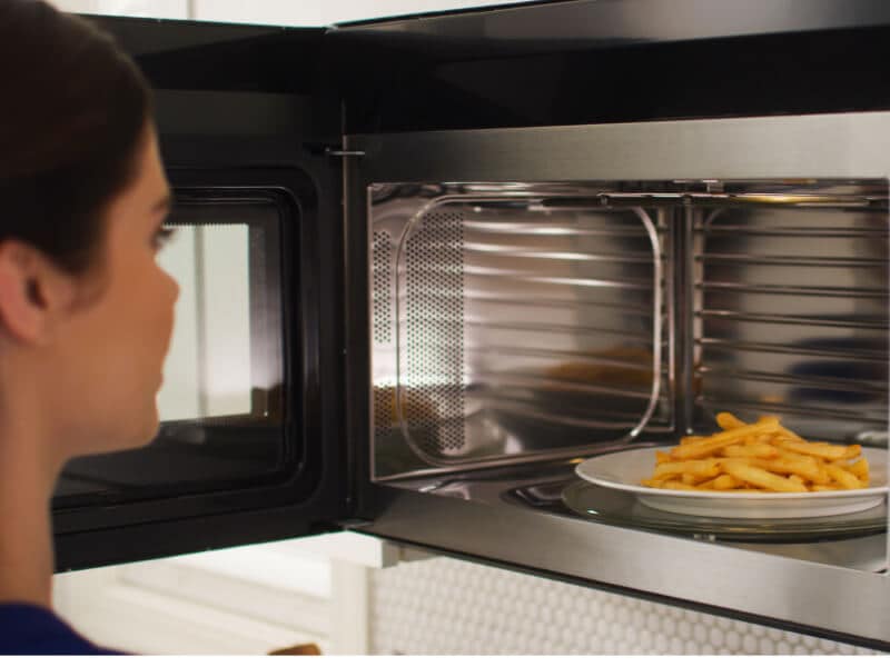 A person removing plate of fries from a microwave A person removing plate of fries from a microwave