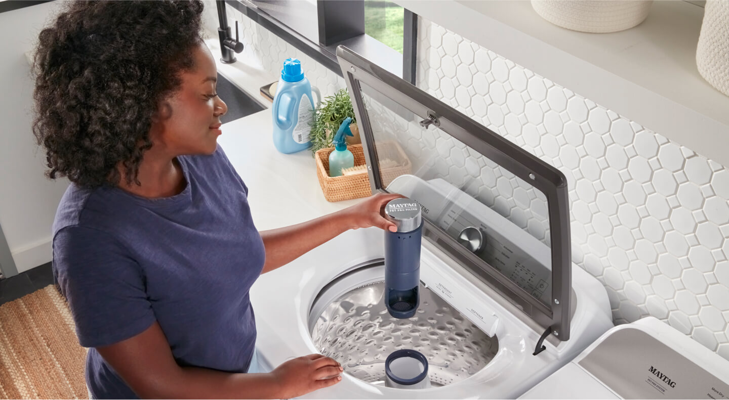 A top view of a person putting the washer filter back into the washer tub