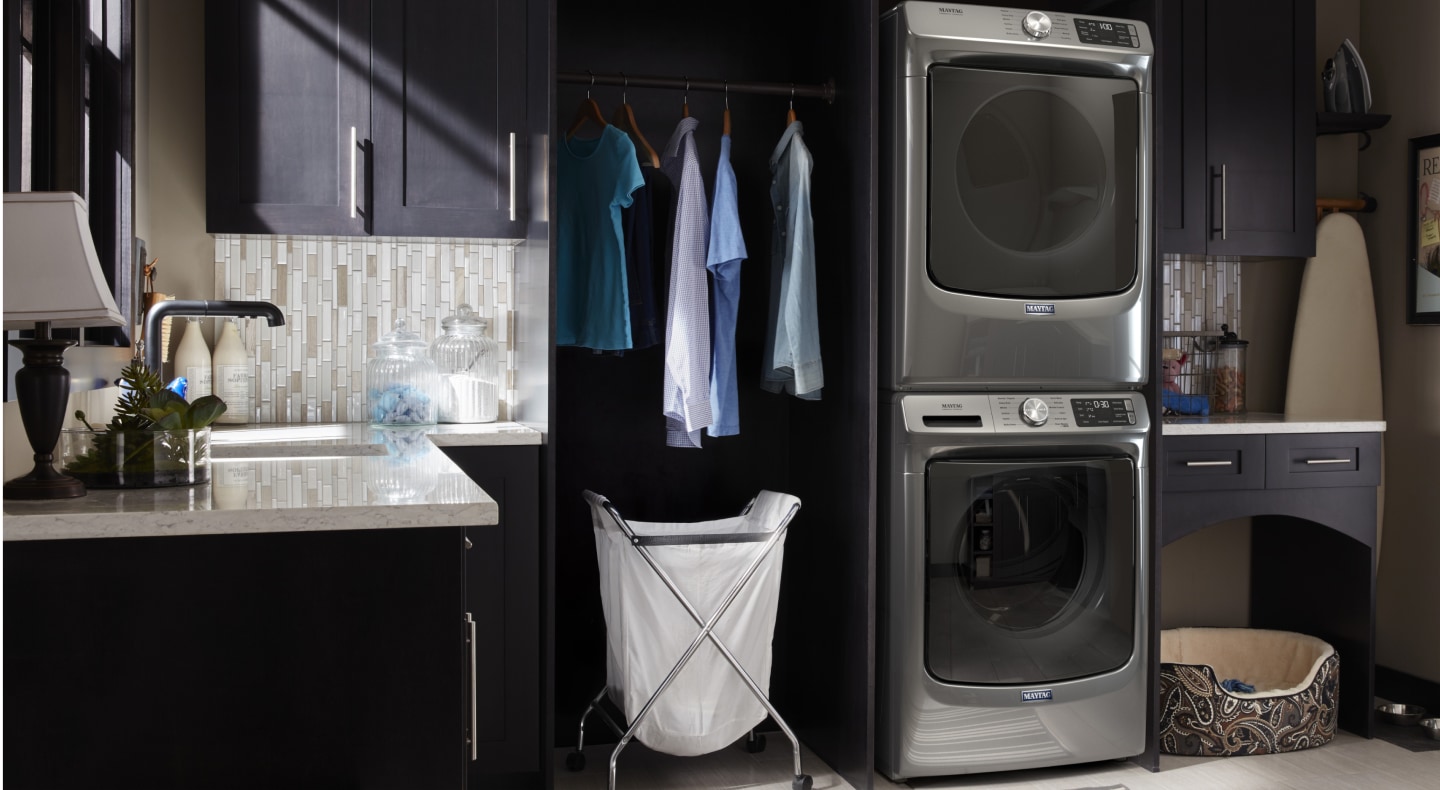 Clothes hanging next to a stacked Maytag® washer and dryer set Clothes hanging next to a stacked Maytag® washer and dryer set