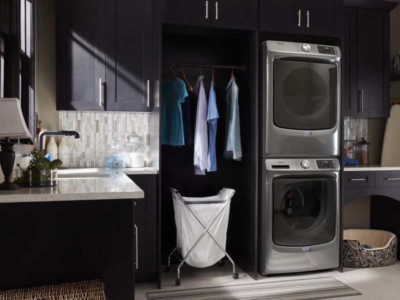 Clothes hanging next to a stacked Maytag® washer and dryer set Clothes hanging next to a stacked Maytag® washer and dryer set