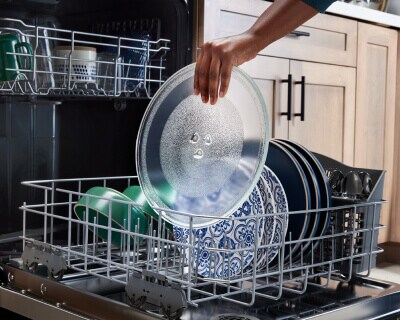 Person placing a microwave turntable in a dishwasher