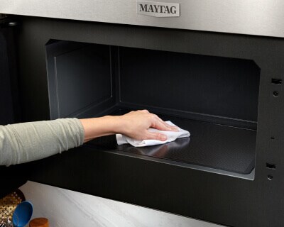 Person wiping down the interior of a Maytag® microwave